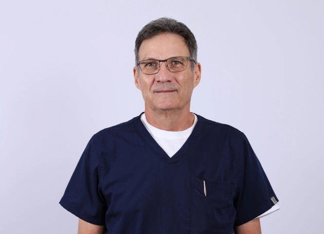 Portrait of Dr. Rusty Sullins at Warwick Dental in Oklahoma City, wearing a blue coat and smiling in the office setting.